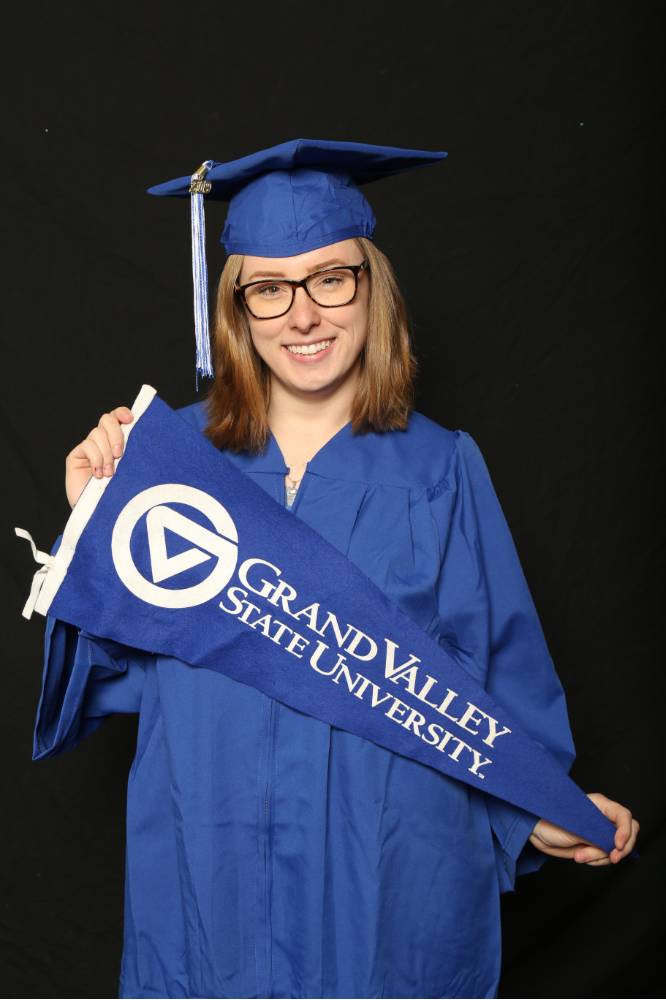 graduate poses with grand valley flag